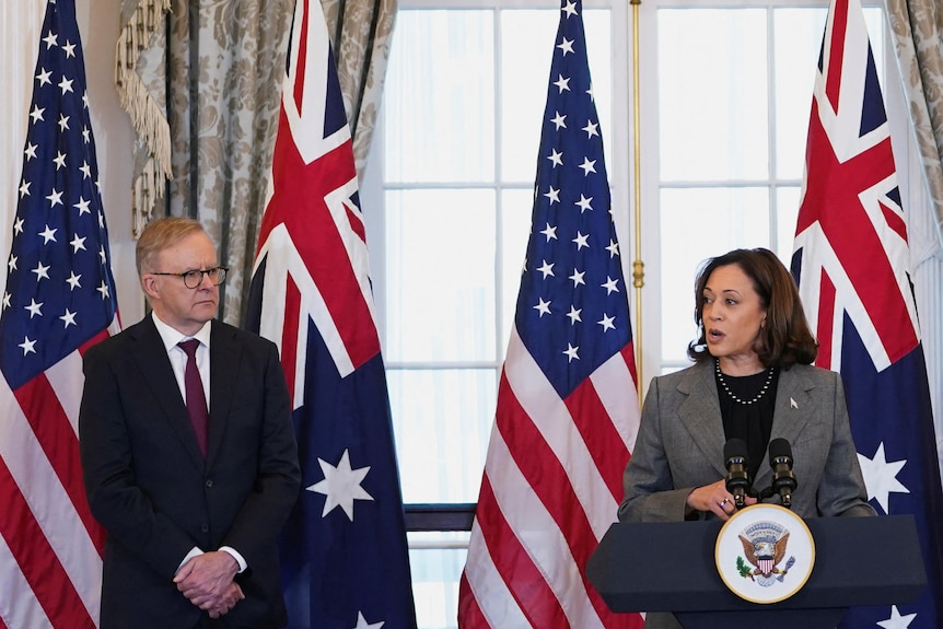 Kamala Harris speaks at a podium with Australian and US flags behind. Anthony Albanese, Antony Blinken are next to her