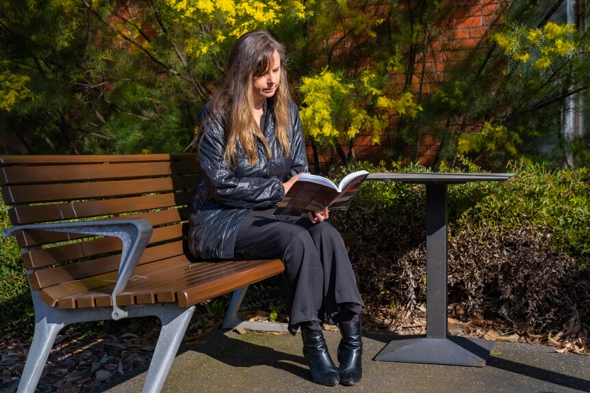 A photo of Anna Halafoff reading on a bench.
