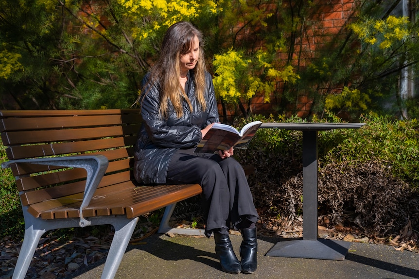 A photo of Anna Halafoff reading on a bench.