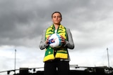 A woman wearing a green and yellow Australia scarf poses with a football