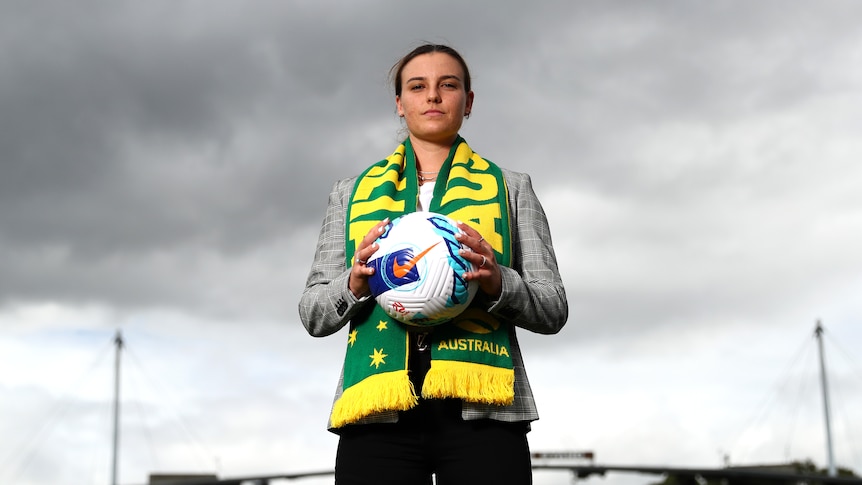 A woman wearing a green and yellow Australia scarf poses with a football