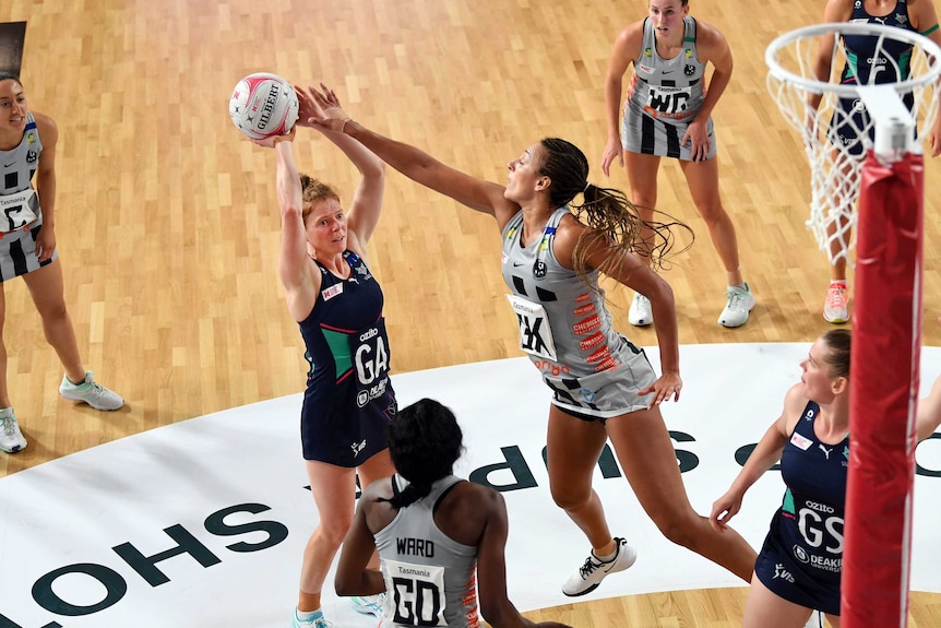 A netballer grimaces as she tries a two-point shot, while a defender stretches her arm out to block.