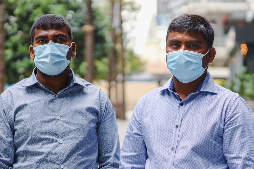 Two men wearing face masks stand side by side.  