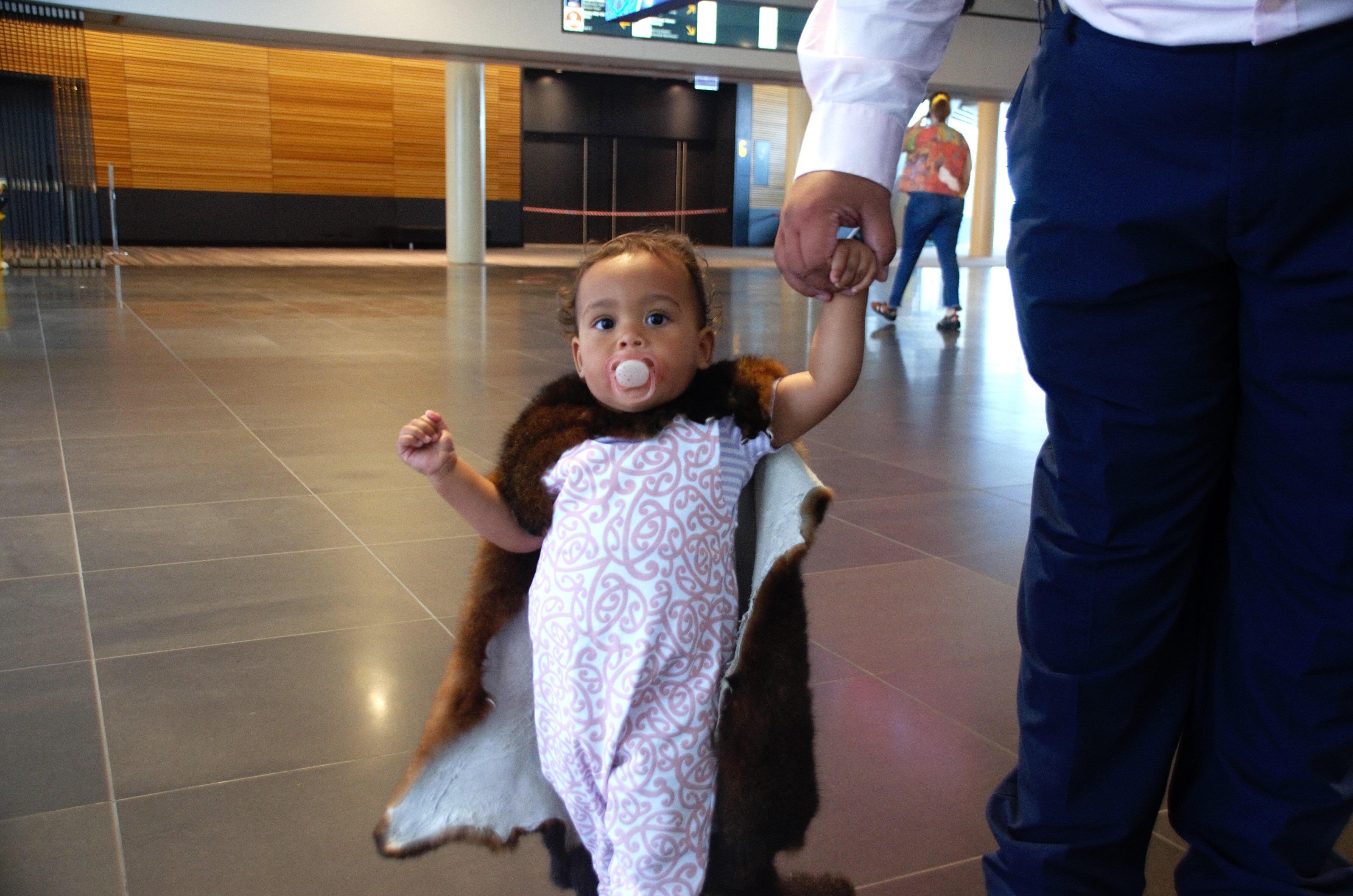 A toddler walks on tiles, holding an adult's hand