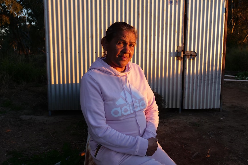 An Aboriginal woman sits in a pink Adidas tracksuit as the sun sets.