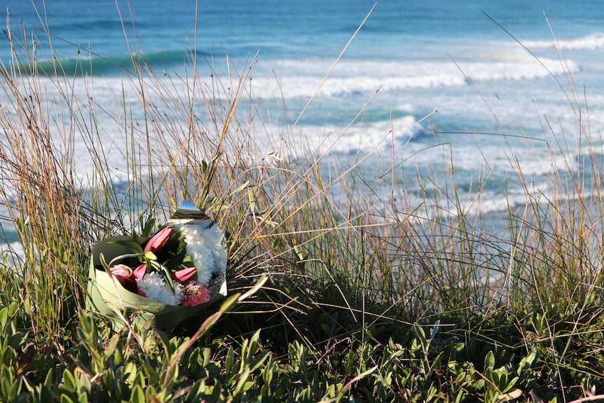 A bunch of flowers left in sand dunes for a shark attack victim in NSW
