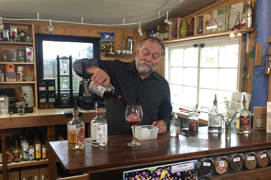 A man standing behind a bar pours a glass of red wine