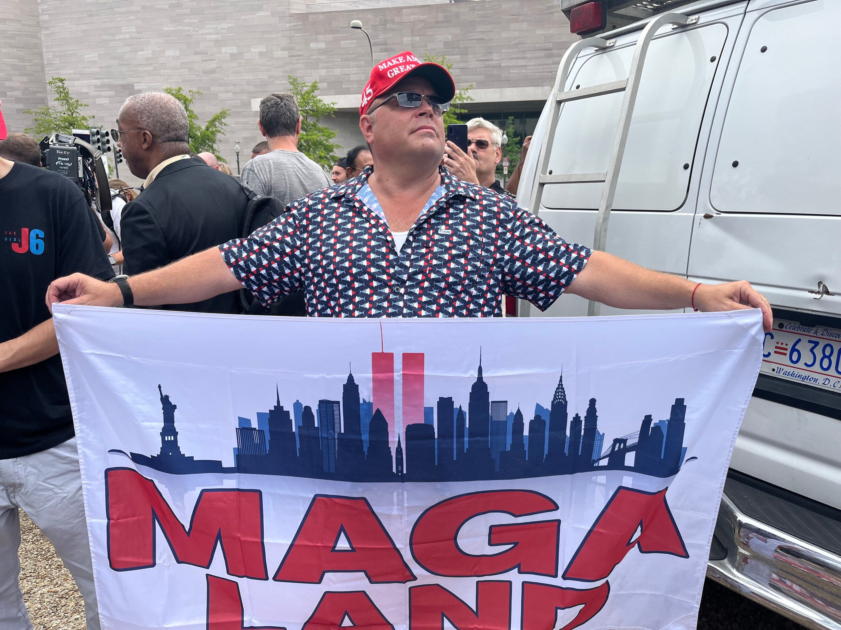 Man with red cap holds up sign saying Maga land 