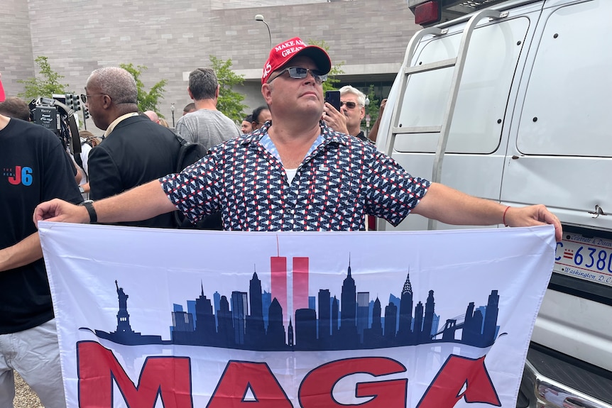 Man with red cap holds up sign saying Maga land 
