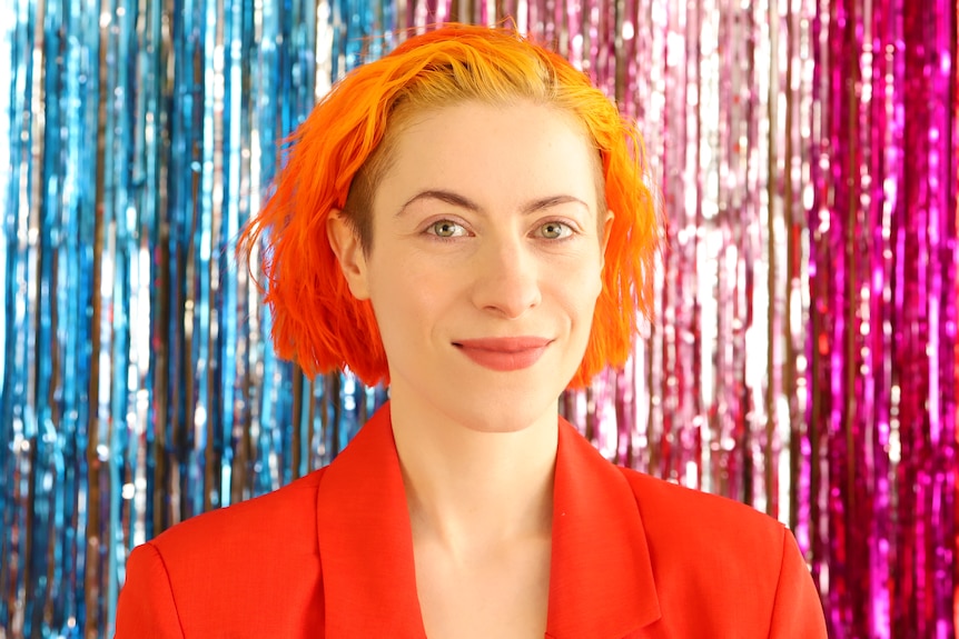 Josie Hess has bright red hair and smiles in front of a colourful background