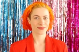 Josie Hess has bright red hair and smiles in front of a colourful background