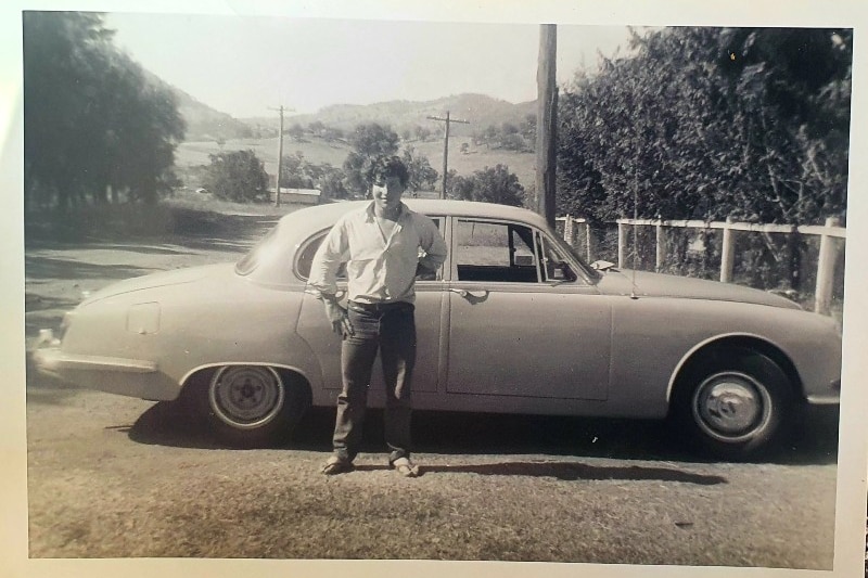 A young man resting on a car in an old black and white photo.