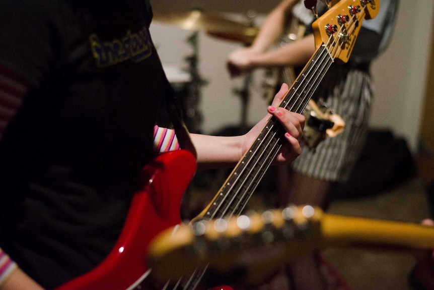 Different people each holding guitars, their faces not shown, with one wearing a Stooges t-shirt