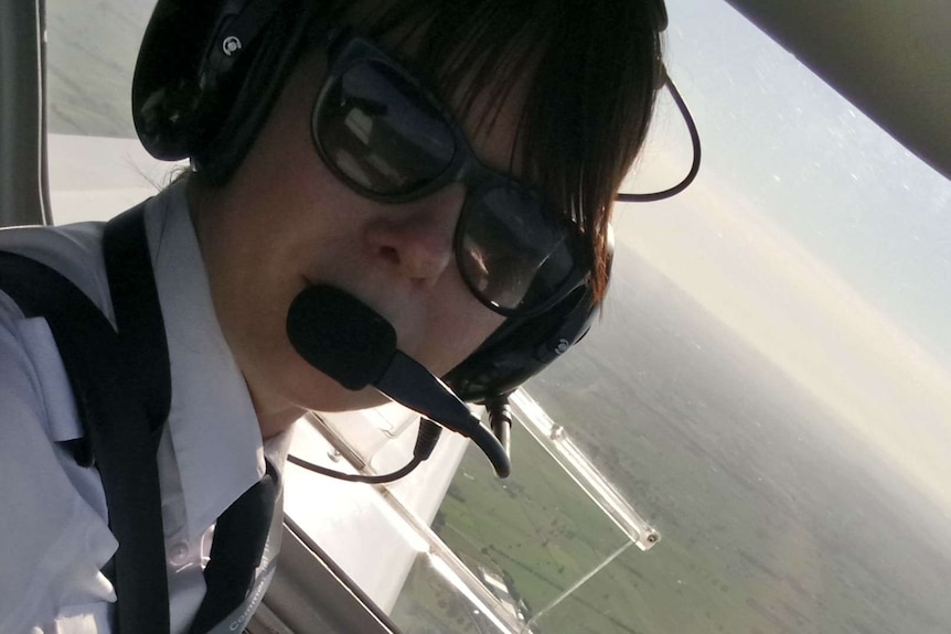 A pilot in the cockpit of a small plane looks at the camera wearing sunglasses.