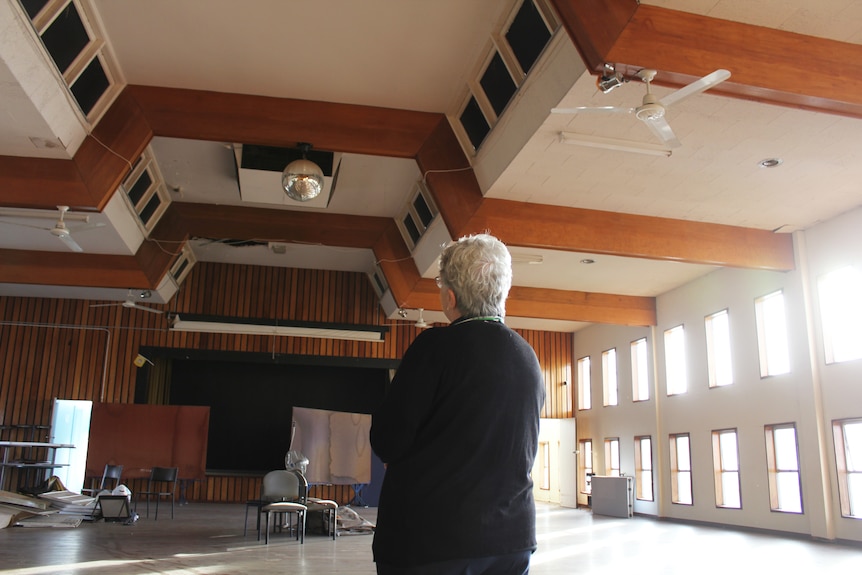 A woman looks up at a disco ball on the ceiling of an empty ballroom