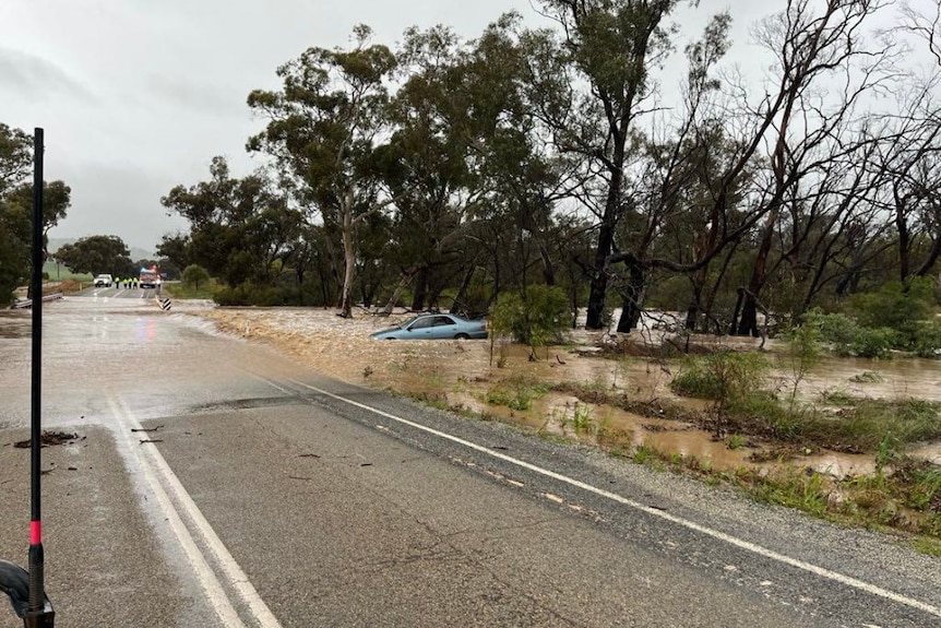 car in floodwater beside a country road that is flooded