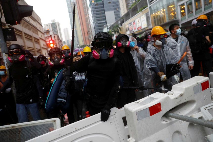 Protesters wearing marks face the camera behind a barricade on the street.