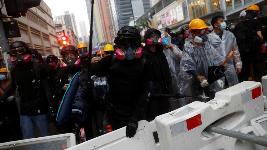 Protesters wearing marks face the camera behind a barricade on the street.