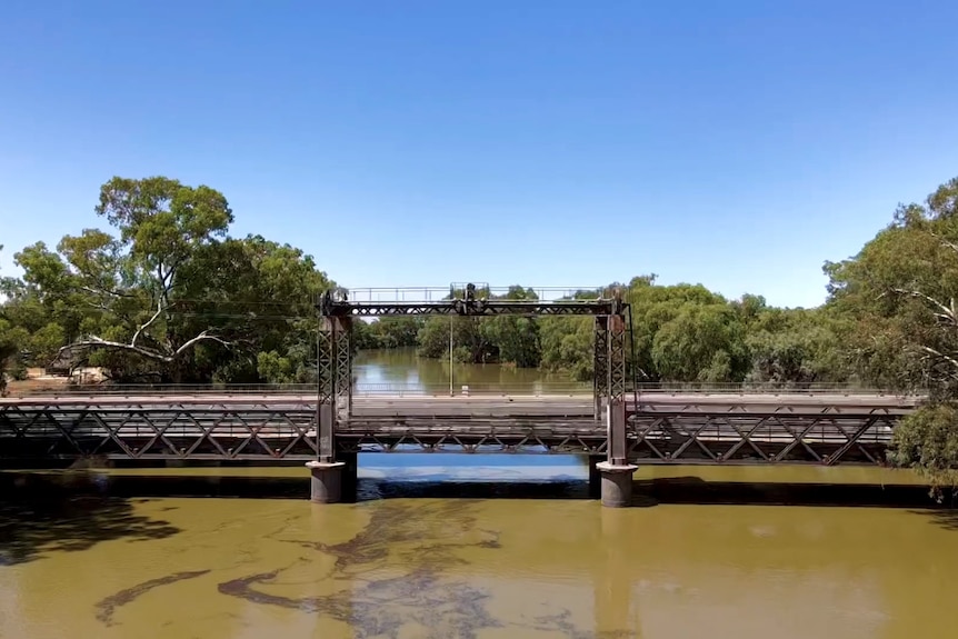 A swollen river running beneath a small bridge.