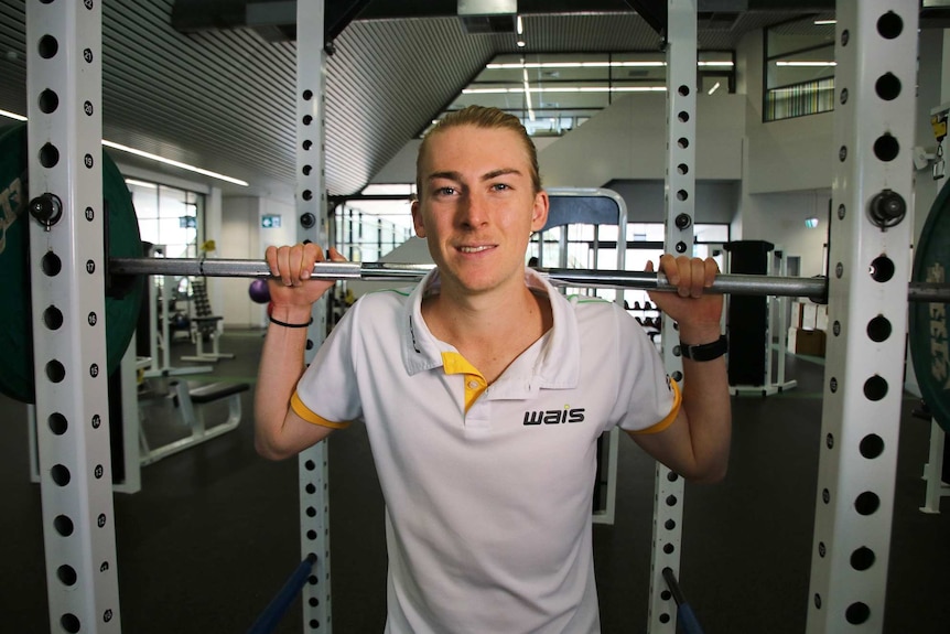 Declan Tingay in the gym holding weights over his shoulders.