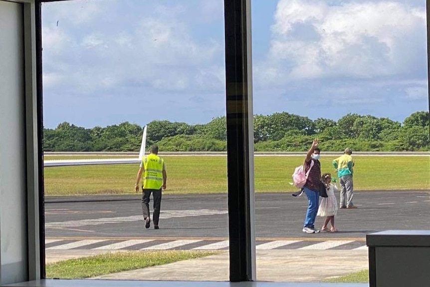 A man and a little girl wave on an airport tarmac.