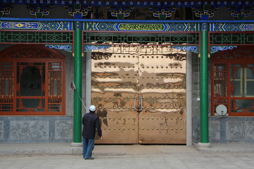 An elderly man cleaning a colourful Chinese mosque