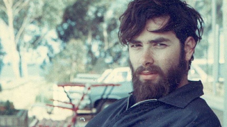 Man with beard and long hair sitting at a table with a milkshake.