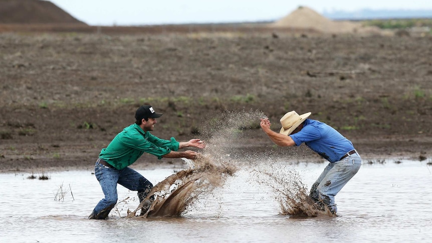 Two farmers splash each other and play in a dam on a rural property.