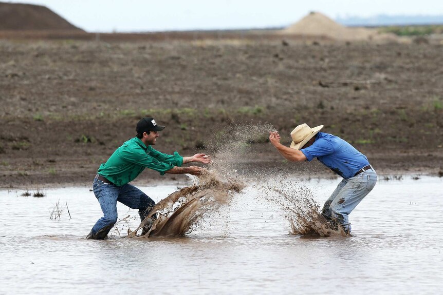 Two farmers splash each other and play in a dam on a rural property.