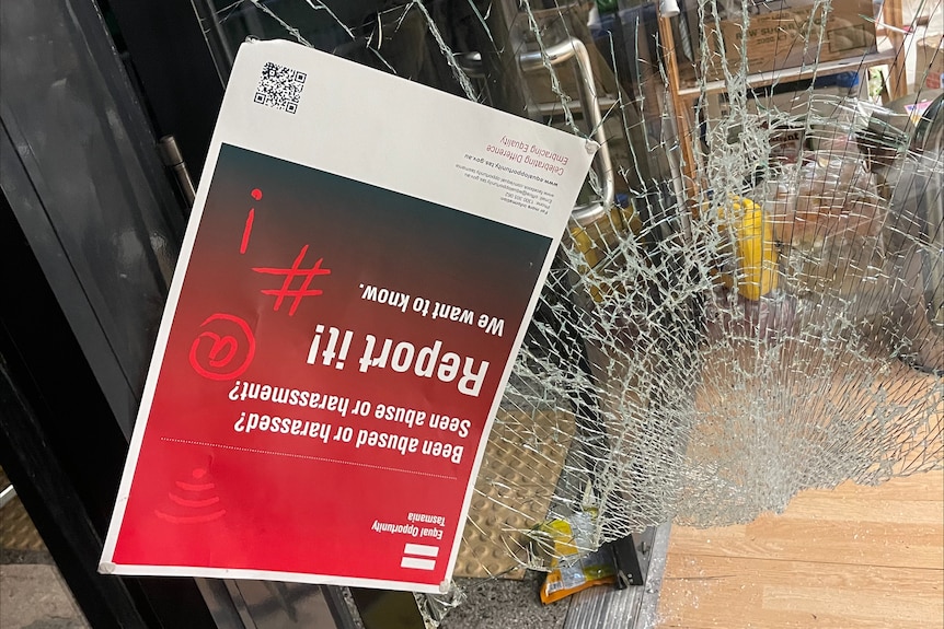 A shattered panel of glass at a Nepalese grocer in Glenorchy, with a poster hanging down
