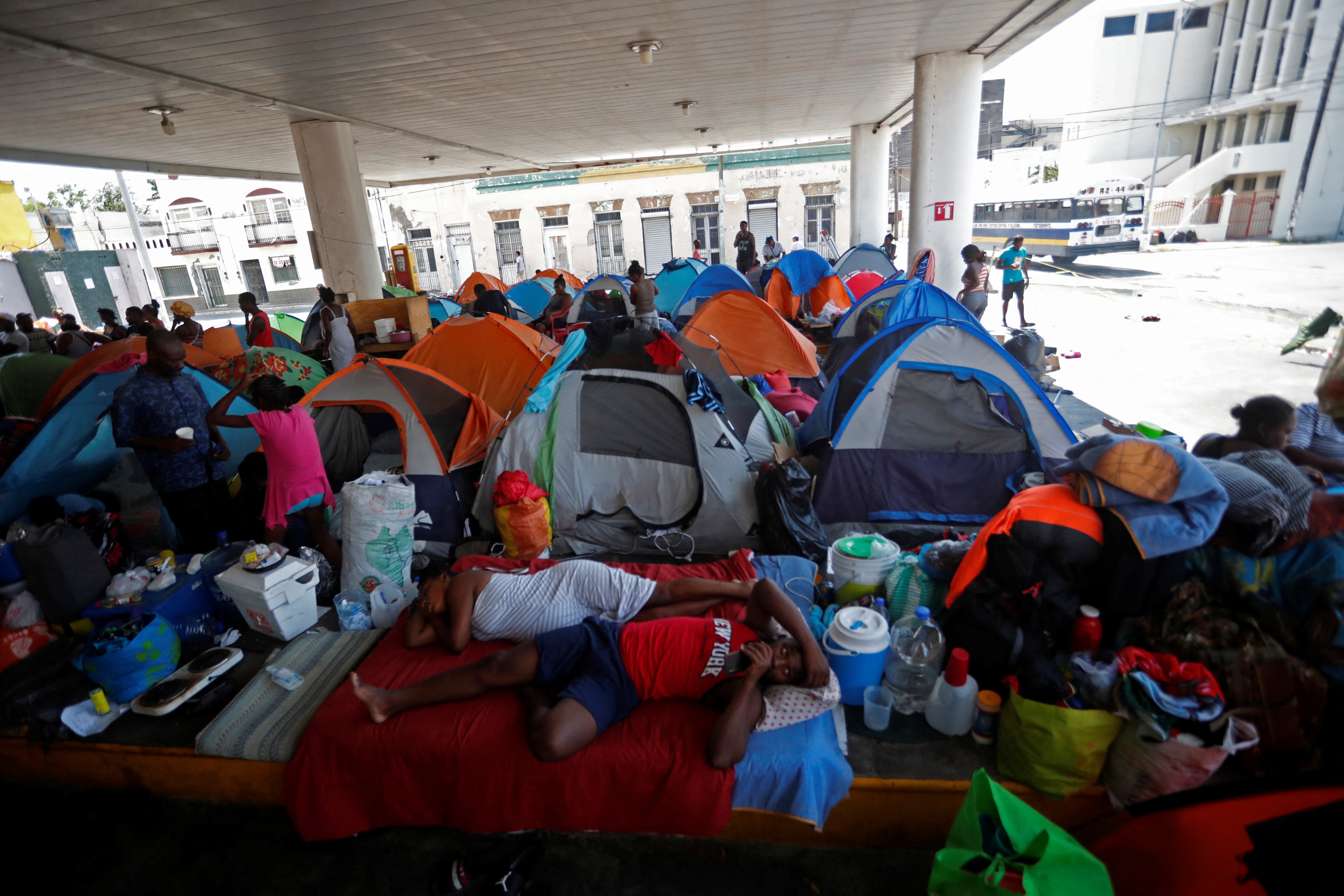 A cluster of tents sit in an abandoned petrol station, with people sprawled on the floor. 