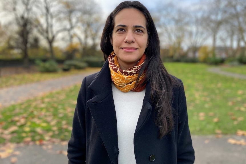 A woman with dark hair stands in a park.