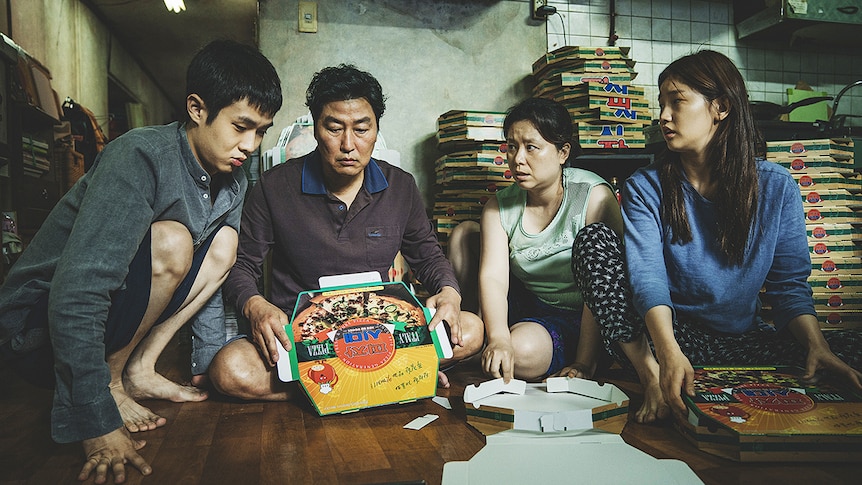 Still of Kang-ho Song, Hyae Jin Chang, Woo-sik Choi, So-dam Park sitting together folding pizza boxes in 2019 film Parasite.