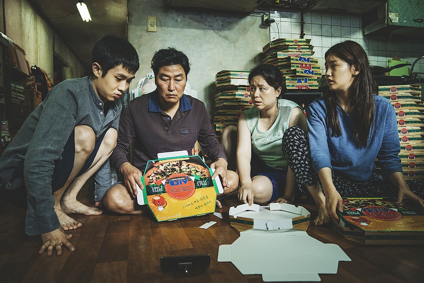 Still of Kang-ho Song, Hyae Jin Chang, Woo-sik Choi, So-dam Park sitting together folding pizza boxes in 2019 film Parasite.