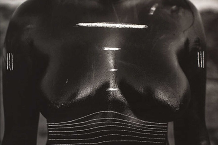 Black and white square cropped image of a woman's nude torso, with lines and patterns scratched onto photograph.