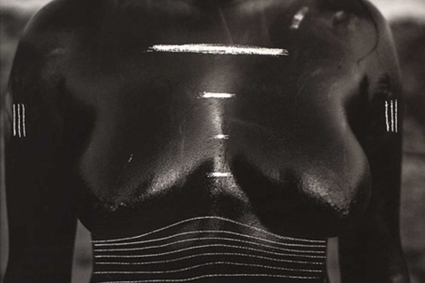 Black and white square cropped image of a woman's nude torso, with lines and patterns scratched onto photograph.