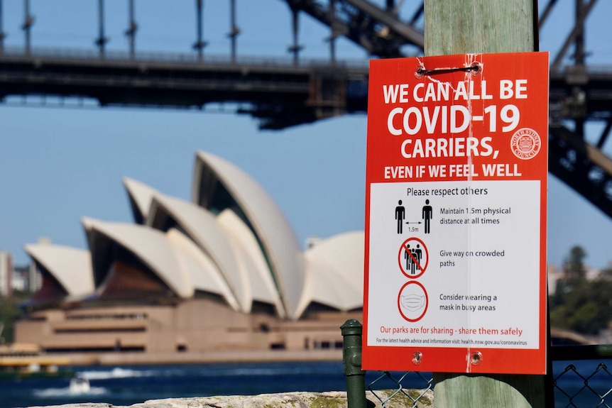 A COVID-19 sign with the Sydney Harbour Bridge and Opera House in the background during lockdown.