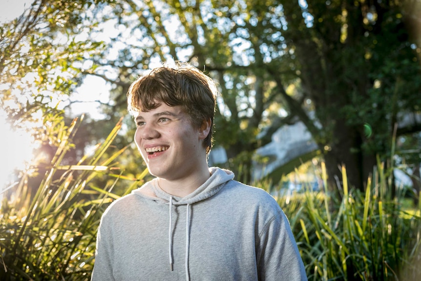 The sun glistens through the leaves as a teenage boy smiles to the distance