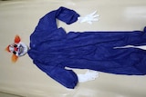 A clown costume - blue jumpsuit, mask and gloves, laid out flat.
