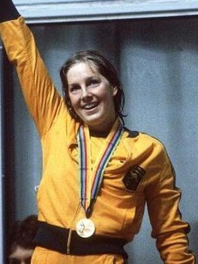 A woman in a yellow tracksuit wearing a gold medal raises her arm in triumph