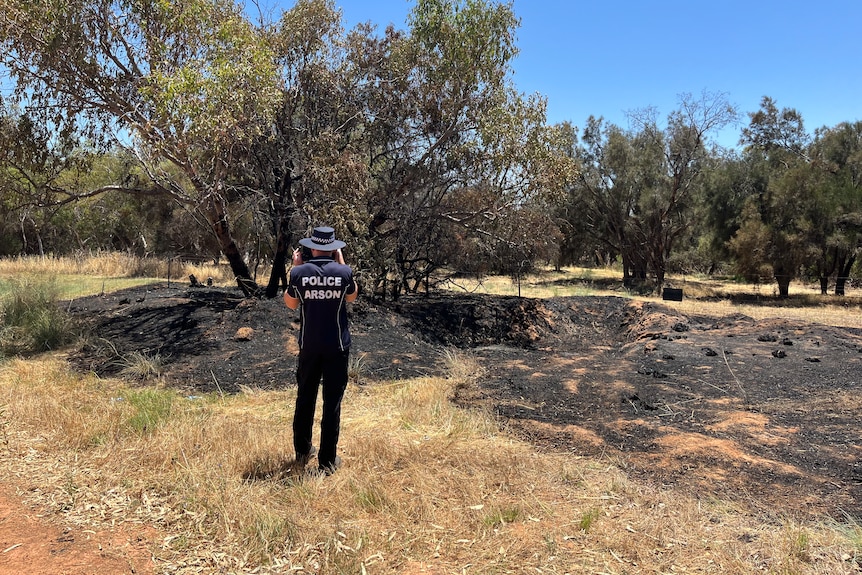 An officer with police arson written on his back takes a photo of scorched forest