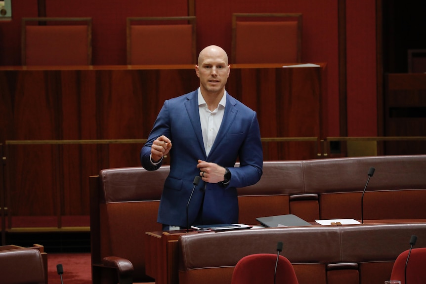 David Pocock, in a suit with no tie, speaking in the Senate behind his table