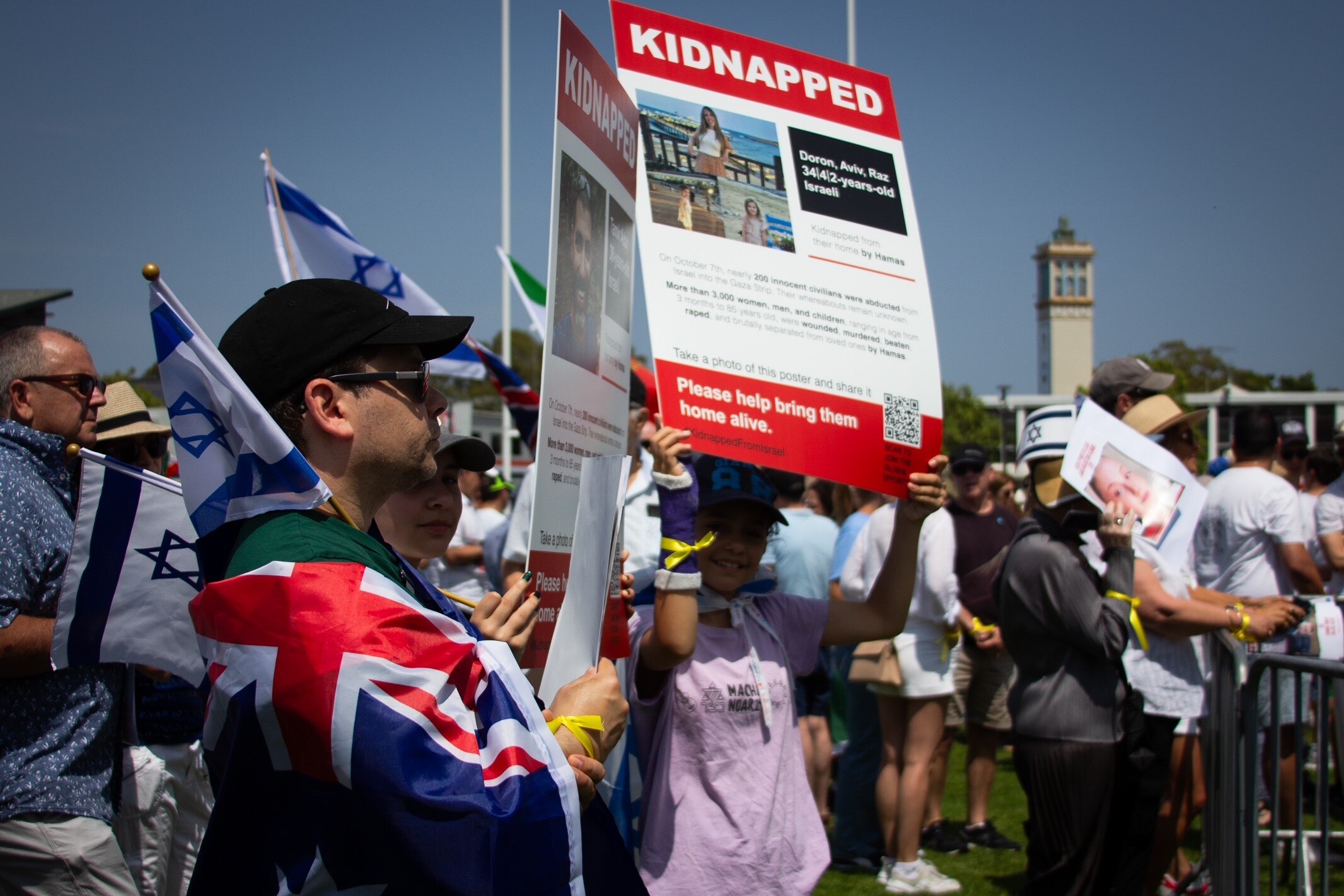 people carrying the israeli flag and posters of those kidnapped by Hamas at a rally in sydney's moore park
