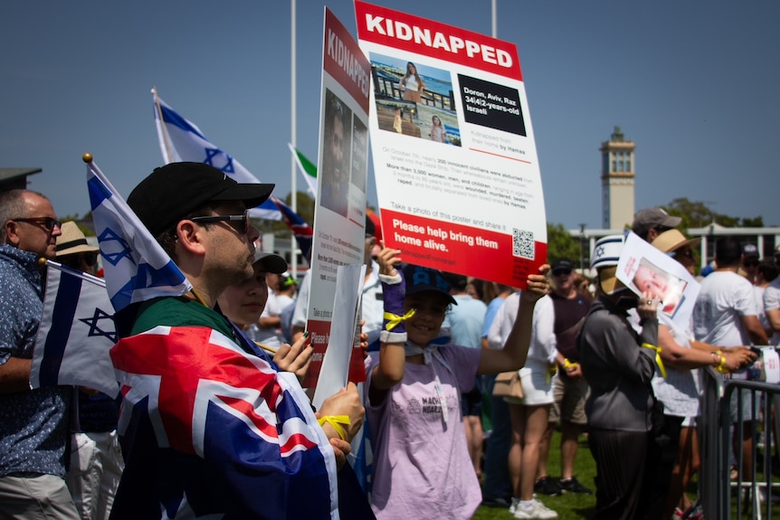 people carrying the israeli flag and posters of those kidnapped by Hamas at a rally in sydney's moore park