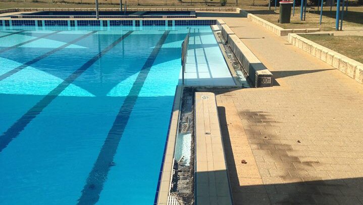 An outdoor swimming pool covered by canopies with damage to its lip caused by vandals.