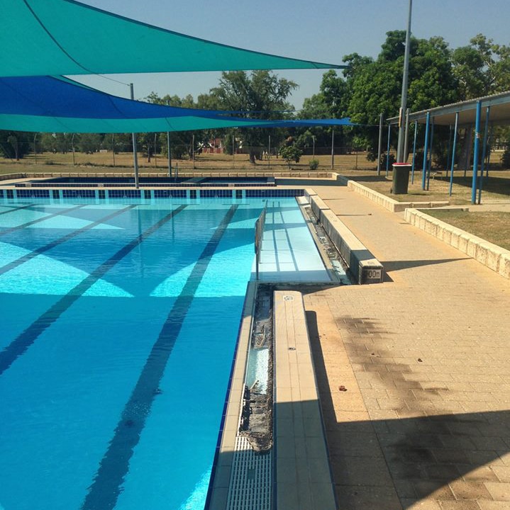 An outdoor swimming pool covered by canopies with damage to its lip caused by vandals.
