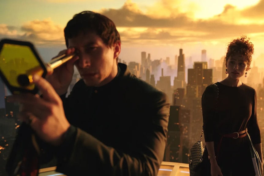 Film still of a man and woman on top of a skyscraper, a city behind them in golden light. Driver peers through a strange device.