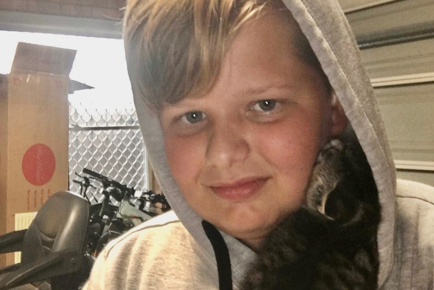 A boy wearing a hoodie hugs a kitten.