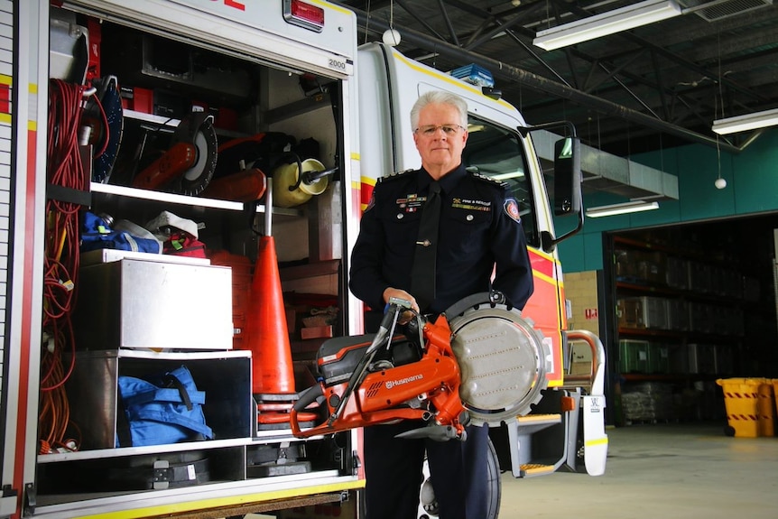 A man holds a steel cutter next to a fire truck.