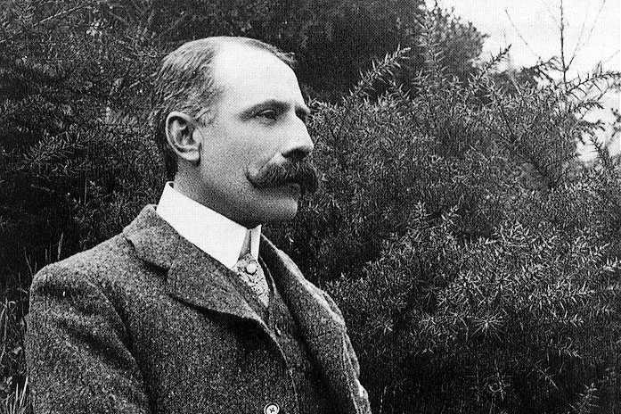 Edward elgar poses with pipe and cane in profile, wearing a smart tweed suit, circa 19000